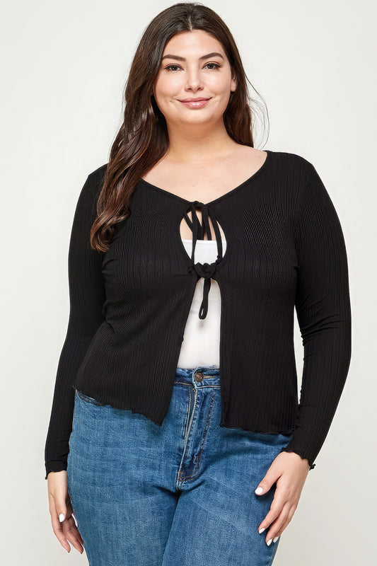 Woman wearing a black long-sleeve top with a tie detail and blue jeans on a white background